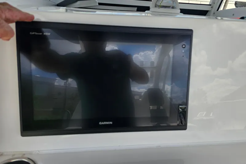  Yacht Photos Pics Garmin display on 2018 Tidewater 320 CC Adventure boat dashboard, reflecting sky and person.