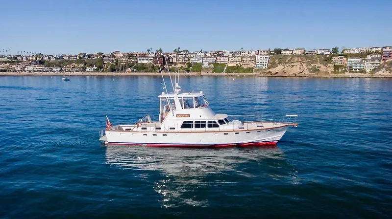 Following Sea Yacht Photos Pics 1965 Bertram 56 yacht cruising on calm waters near a coastal town.