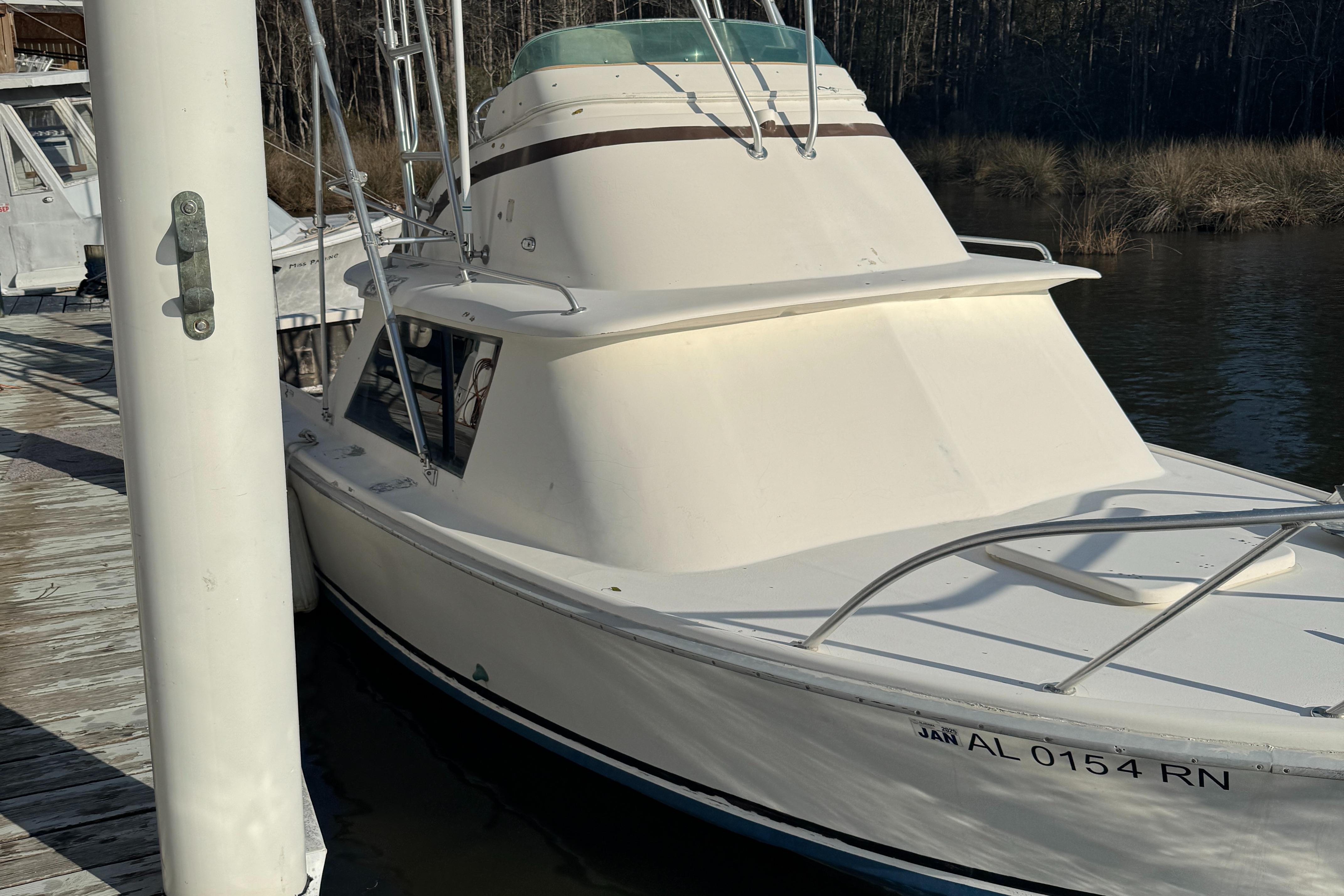 1974 Bertram 31 Flybridge boat docked, side view, white exterior, calm water background.