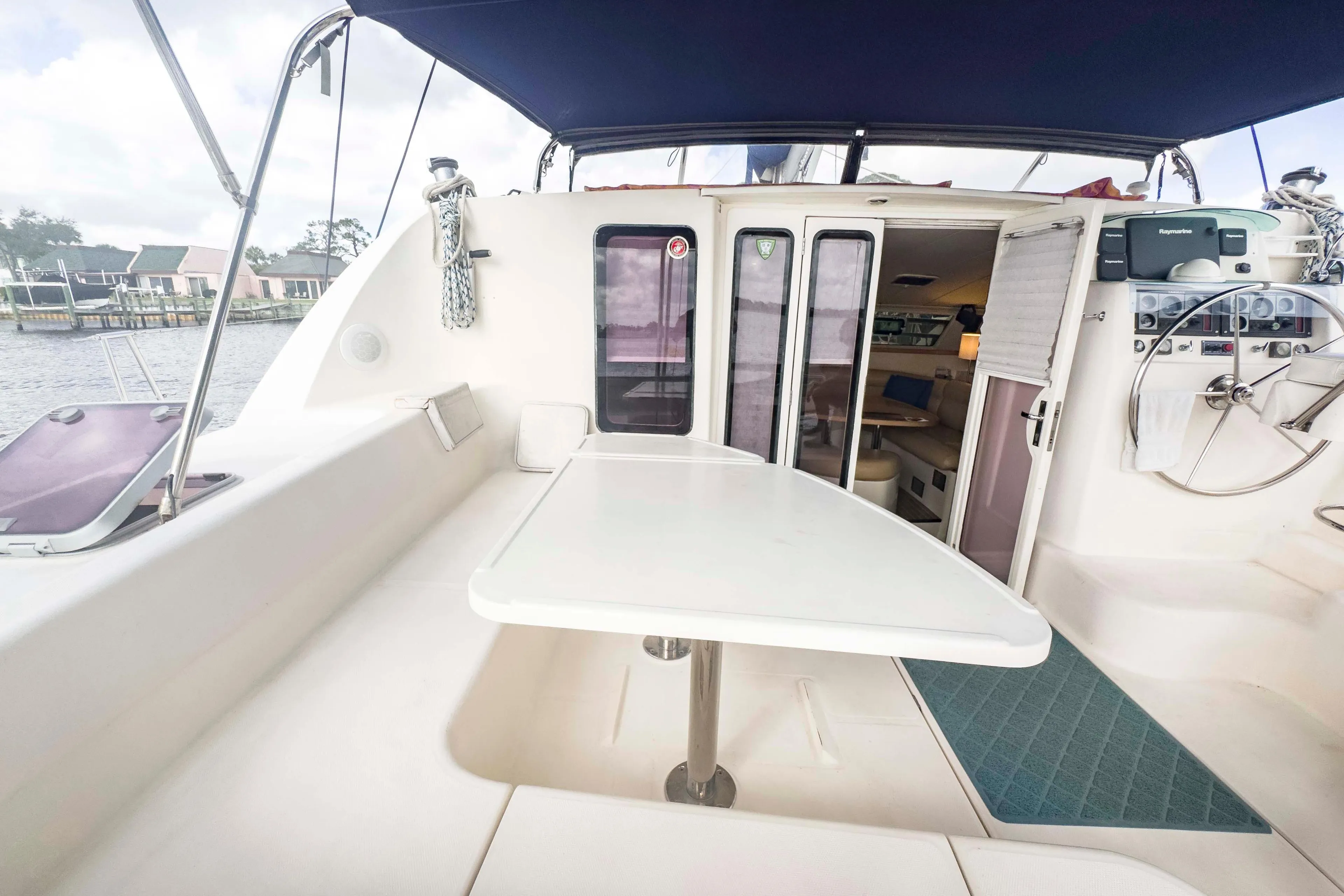 2002 Leopard 42 catamaran cockpit with table, seating, and helm, docked by waterfront homes.