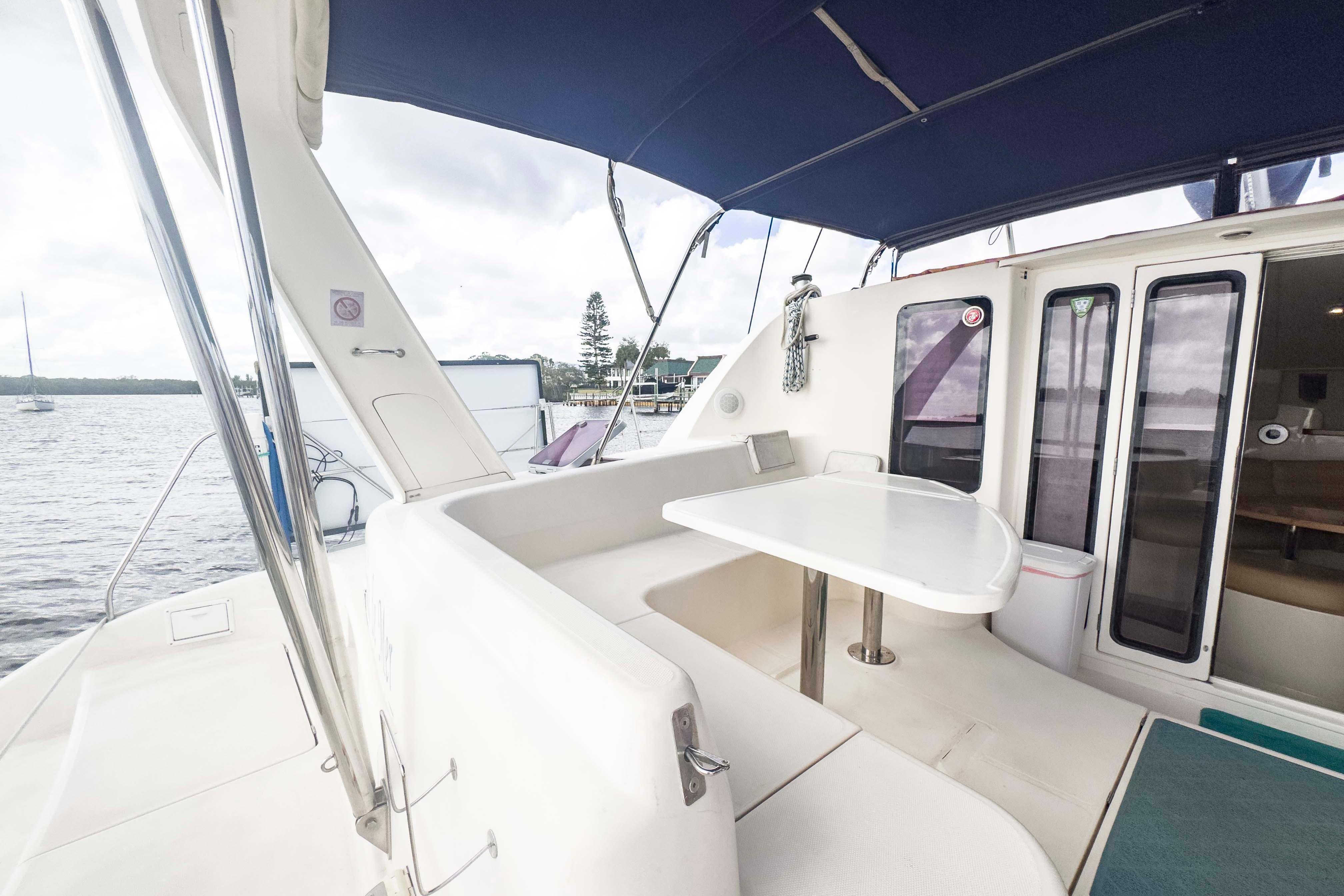 Spacious deck of 2002 Leopard 42 catamaran with seating and table, docked by the water.