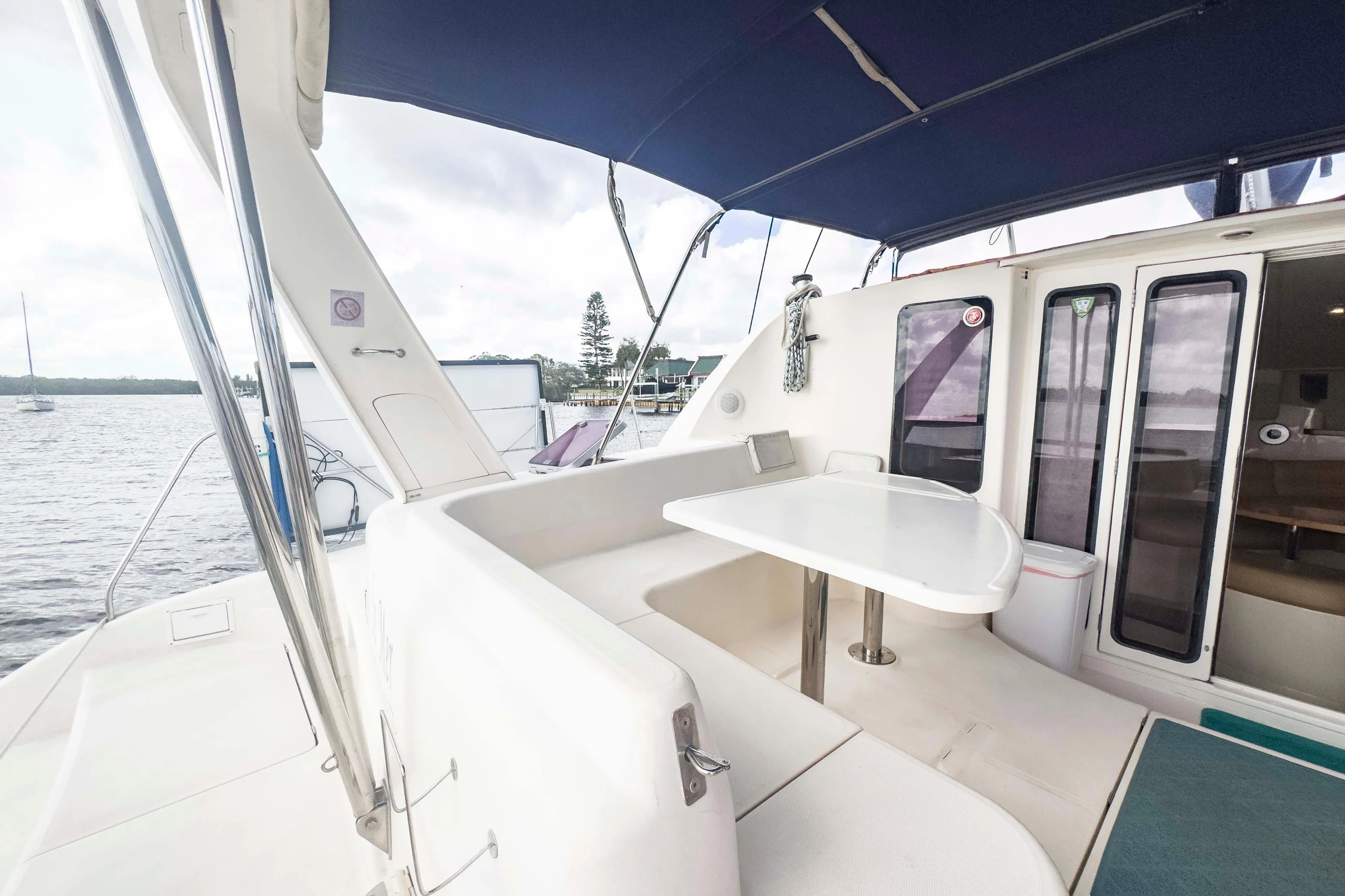 Spacious deck of 2002 Leopard 42 catamaran with seating and table, docked by the water.
