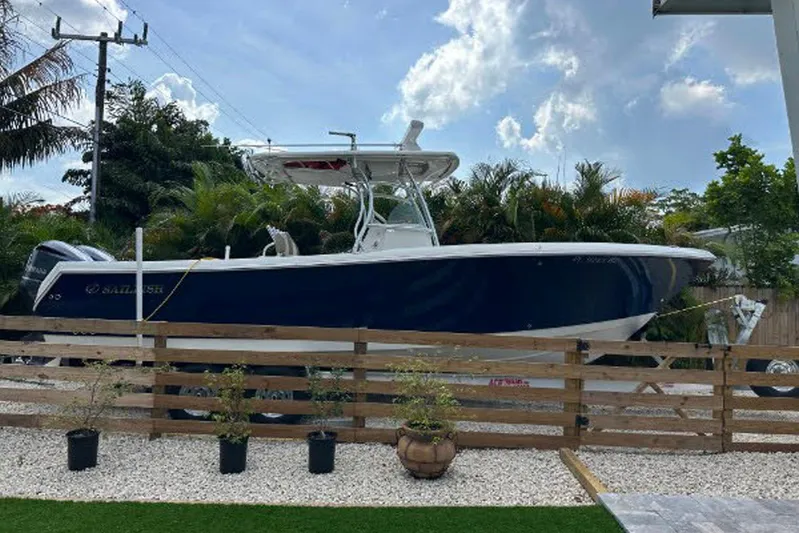 Buddy Yacht Photos Pics 2013 Sailfish 290 CC boat parked outdoors, surrounded by greenery and a wooden fence.