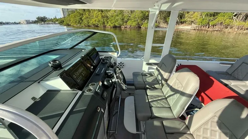 No Name Yacht Photos Pics 2019 Axopar 37 Sun Top boat interior with modern dashboard and seating, near lush shoreline.