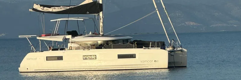 Samcat Yacht Photos Pics 2020 Lagoon 46 catamaran sailing on calm waters with mountainous backdrop.
