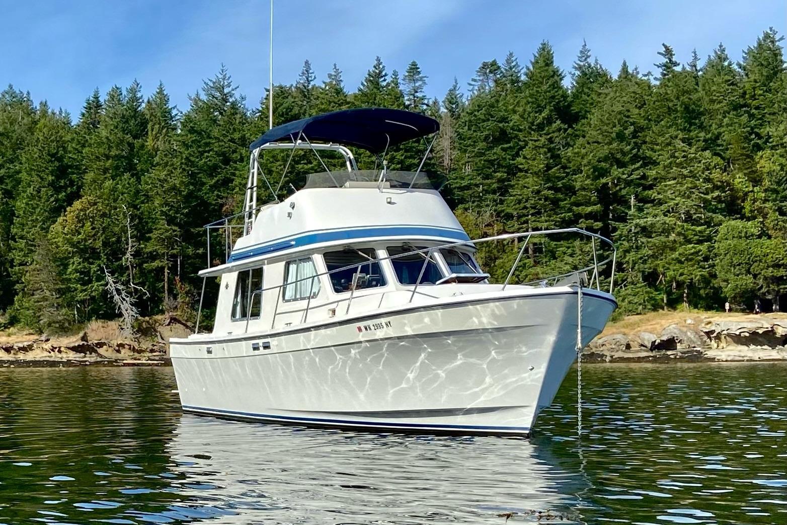 1986 Lynnwood Flybridge Sedan boat on calm water with forested shoreline background.