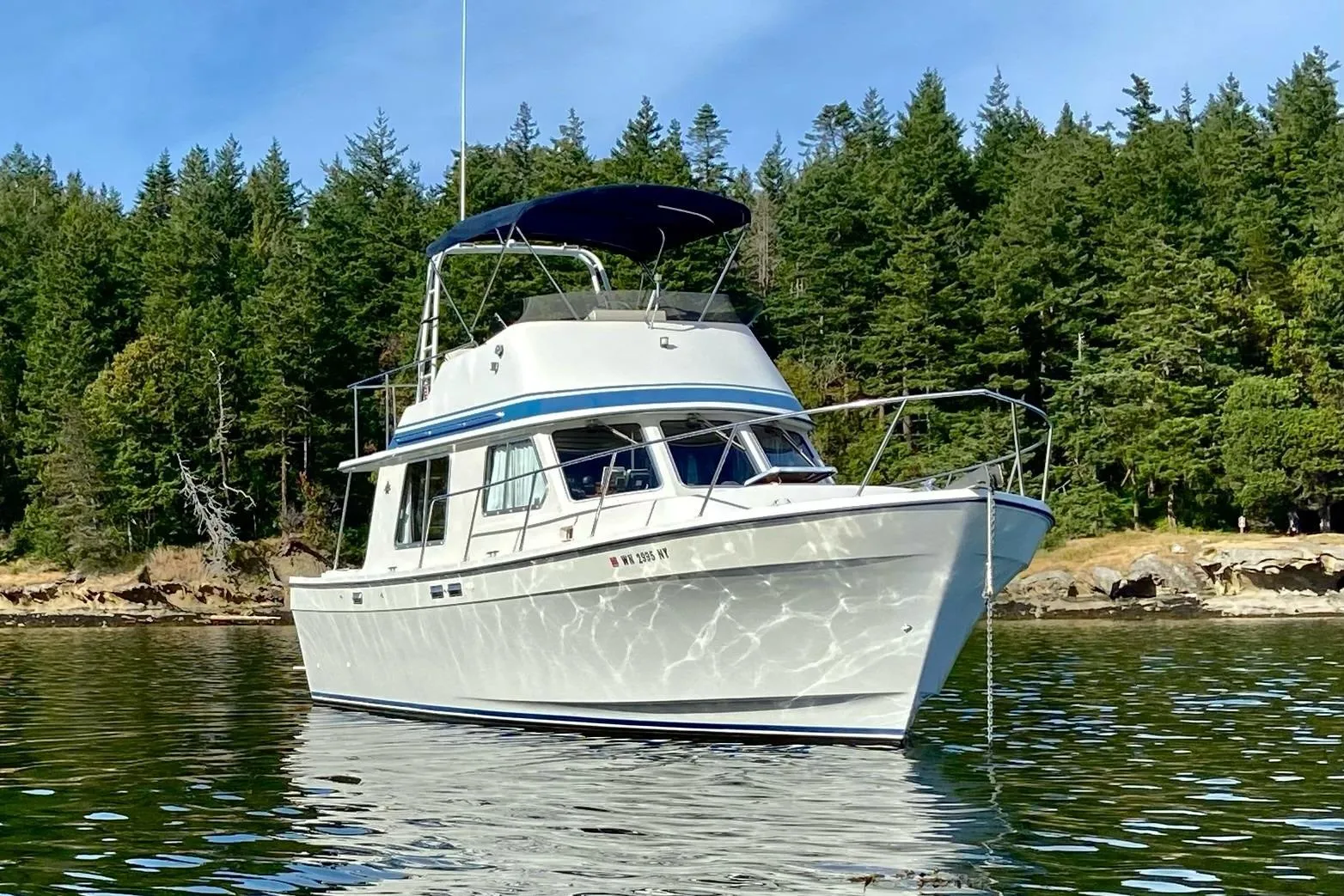 1986 Lynnwood Flybridge Sedan boat on calm water with forested shoreline background.