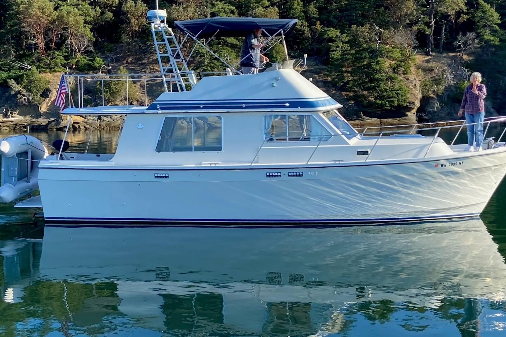 1986 Lynnwood Flybridge Sedan boat on calm water with scenic forest backdrop.
