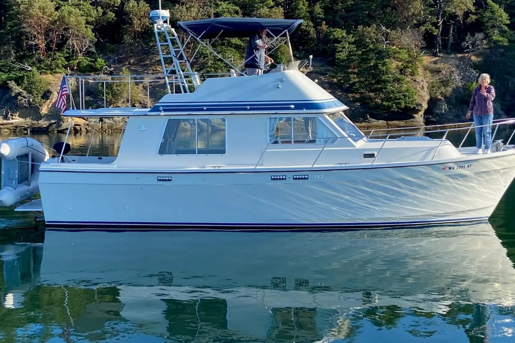 1986 Lynnwood Flybridge Sedan boat on calm water with scenic forest backdrop.