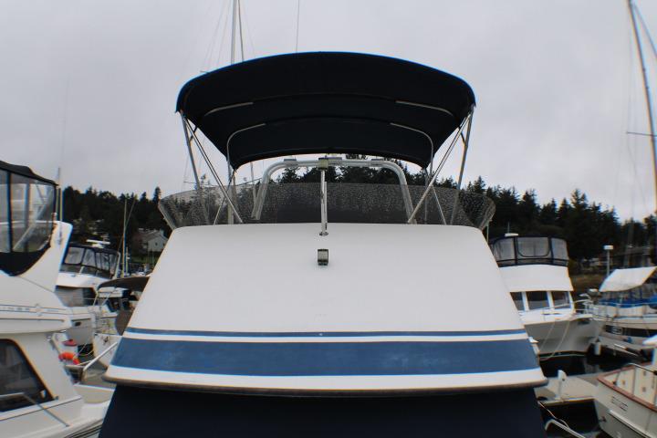 1986 Lynnwood Flybridge Sedan boat docked at marina, featuring blue canopy and sleek design.