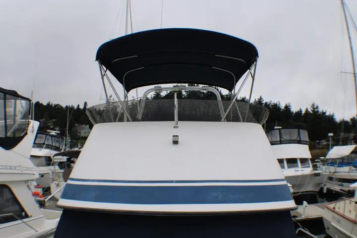 1986 Lynnwood Flybridge Sedan boat docked at marina, featuring blue canopy and sleek design.