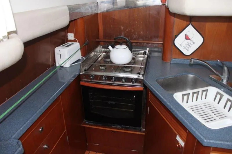 Mangata Yacht Photos Pics Compact kitchen area in a 2003 Lagoon 43 PC yacht with stove, sink, and kettle.