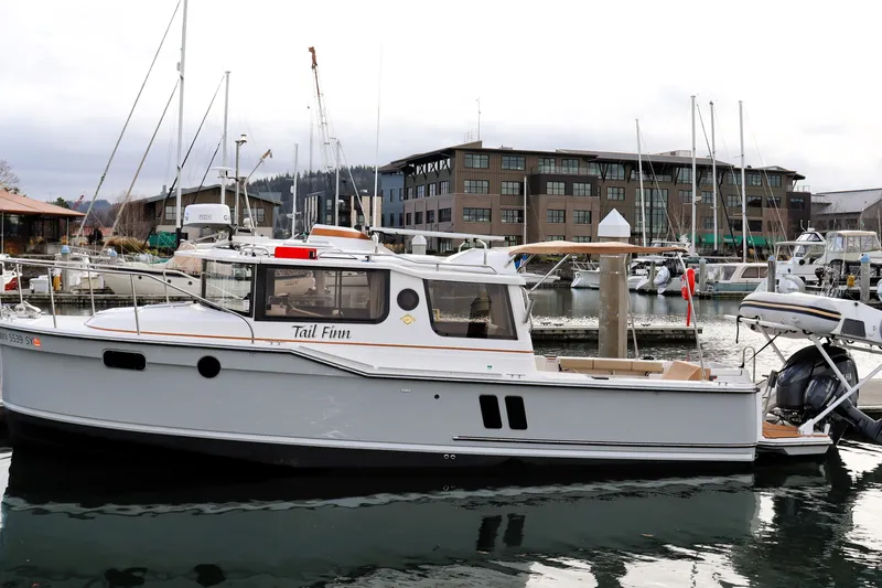 Tail Finn Yacht Photos Pics 2021 Ranger Tugs R-27 boat docked in a marina with modern buildings in the background.