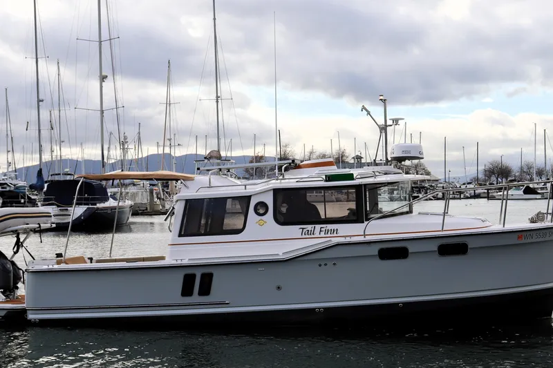 Tail Finn Yacht Photos Pics 2021 Ranger Tugs R-27 boat docked in a marina with sailboats in the background.