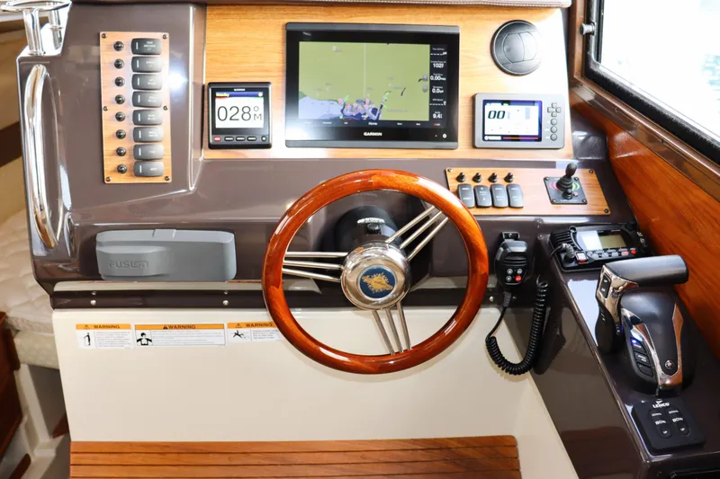 Tail Finn Yacht Photos Pics 2021 Ranger Tugs R-27 helm with navigation screens, wooden steering wheel, and control panel.