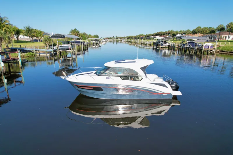  Yacht Photos Pics 2020 Beneteau Antares 9 OB boat on a calm canal, surrounded by docks and palm trees.