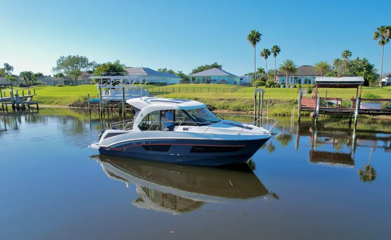  Yacht Photos Pics 2020 Beneteau Antares 9 OB boat on calm water, surrounded by lush greenery and houses.