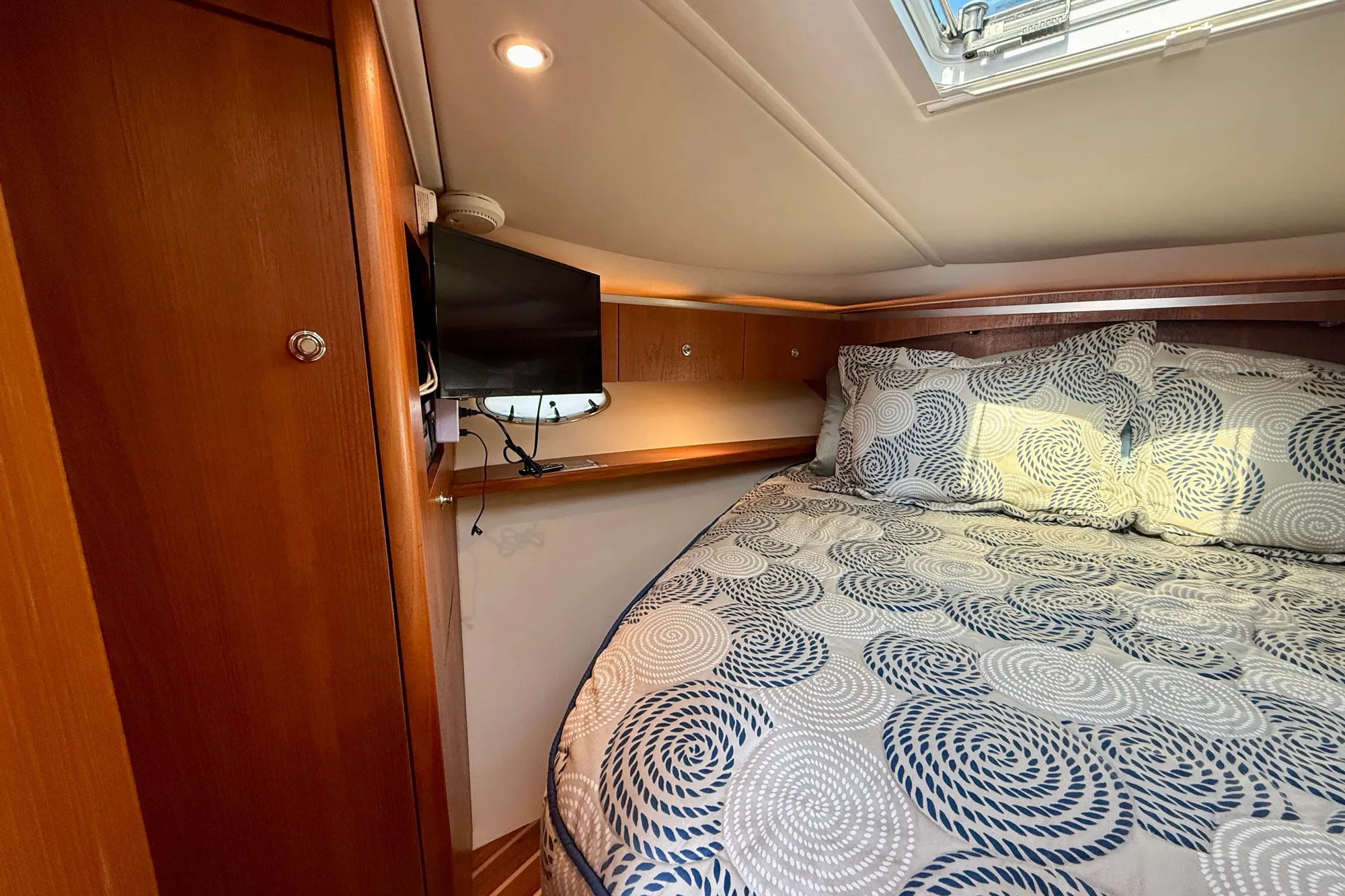 Cozy cabin interior of 2005 Tiara 3600 Open with patterned bedding and wall-mounted TV.