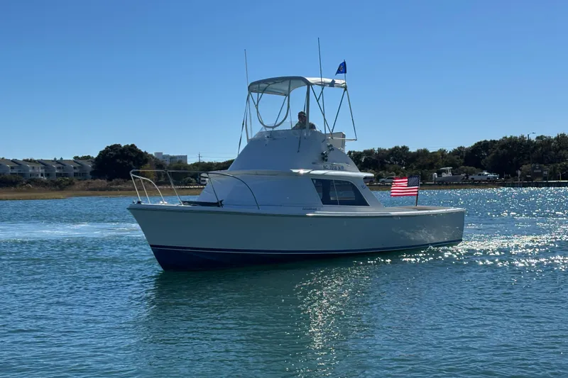 Bandit Yacht Photos Pics 1970 Bertram 31 Flybridge Cruiser on calm water, American flag waving.