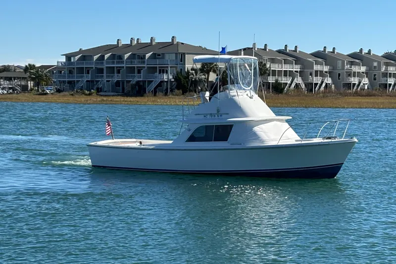 Bandit Yacht Photos Pics 1970 Bertram 31 Flybridge Cruiser on water near waterfront homes, clear sky.