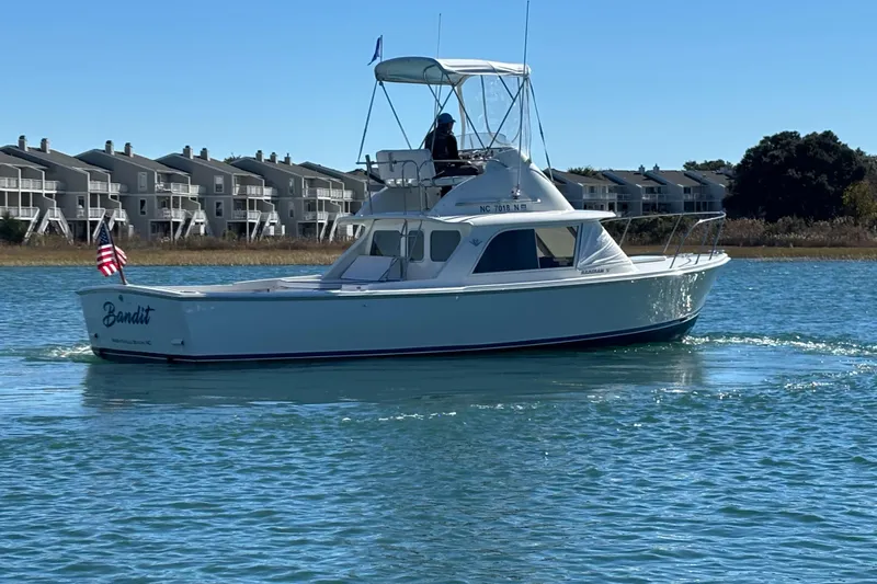 Bandit Yacht Photos Pics 1970 Bertram 31 Flybridge Cruiser on water, with American flag, near waterfront homes.
