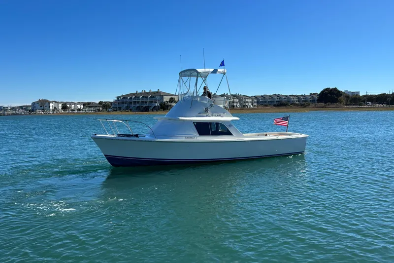 Bandit Yacht Photos Pics 1970 Bertram 31 Flybridge Cruiser on calm water, American flag, clear blue sky.