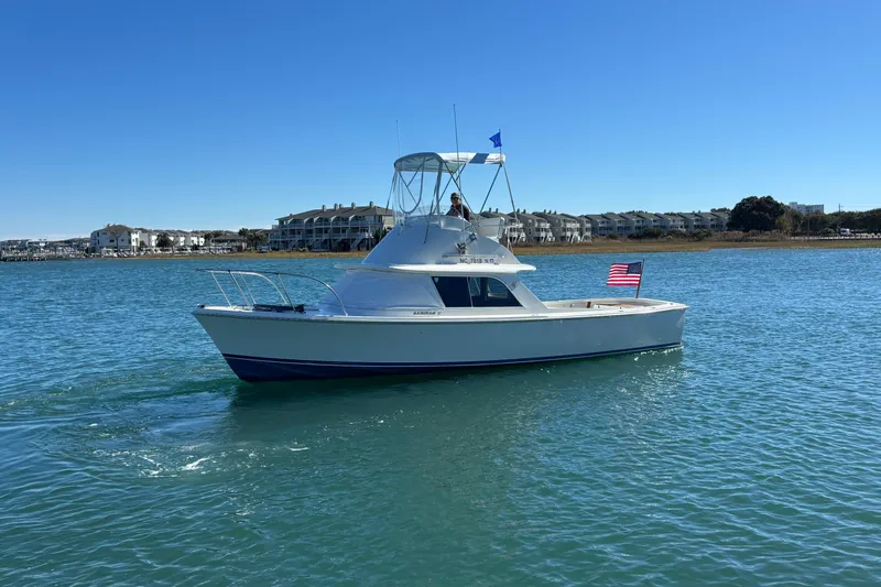 Bandit Yacht Photos Pics 1970 Bertram 31 Flybridge Cruiser on calm water, clear sky, American flag displayed.
