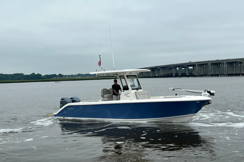 Happy Hours Yacht Photos Pics 2023 Pursuit S 268 Sport boat cruising on a calm river near a bridge.
