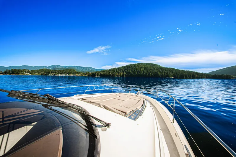 Luna Maris Yacht Photos Pics Prestige 550 yacht cruising on a serene lake with forested hills, under a clear blue sky.