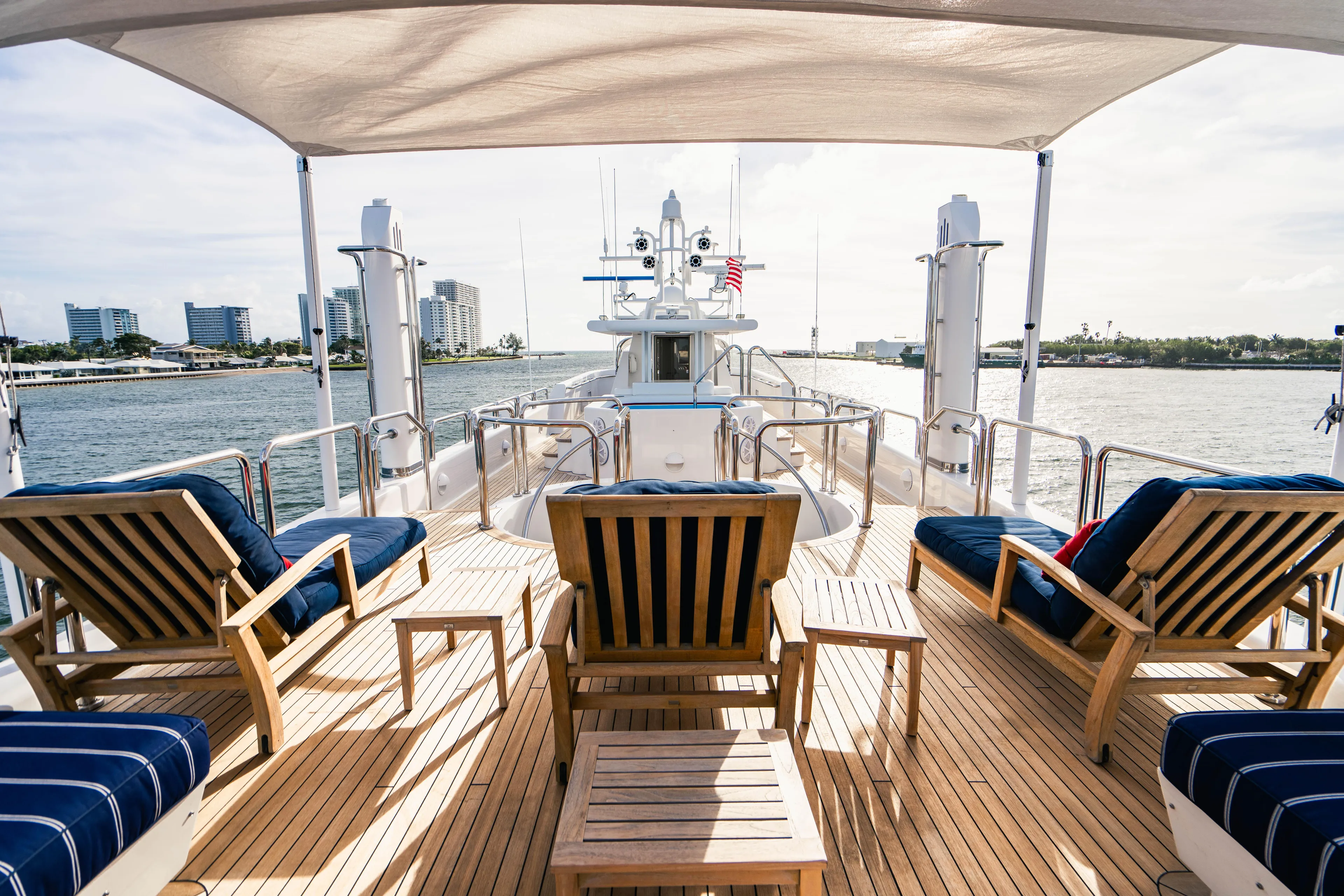 High Occupancy Yacht Photos Pics Luxury Oceanfast Custom yacht deck with wooden chairs, ocean view, and modern cityscape in the background.