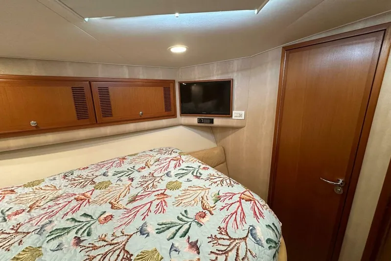 Merry Yacht Yacht Photos Pics 2004 Cabo 48 Flybridge cabin with floral bedding, wooden cabinets, and a wall-mounted TV.