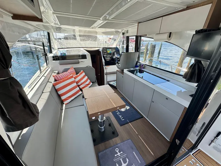  Yacht Photos Pics 2024 Beneteau Antares 11 interior with seating, table, and helm, overlooking marina.