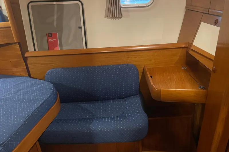"dragonfly" Yacht Photos Pics Interior of 2003 Jeanneau Sun Odyssey 43 DS with blue seating and wooden desk.