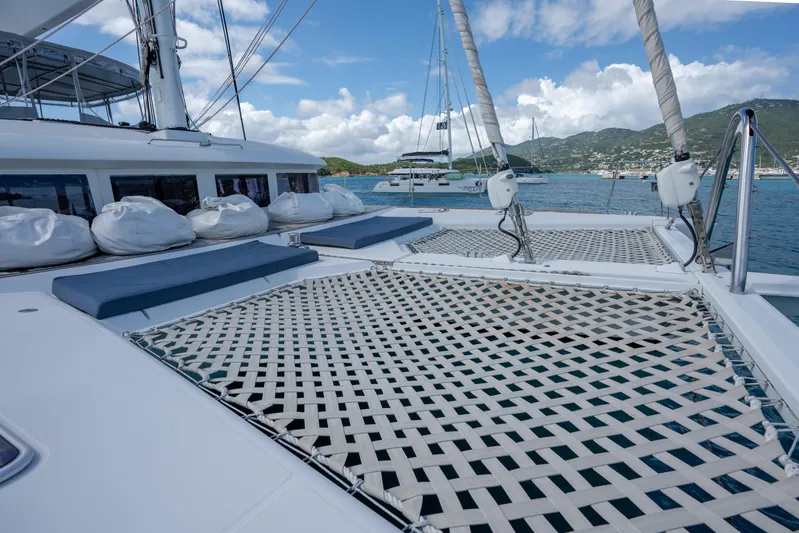  Yacht Photos Pics Catamaran Lagoon 620, 2014 model, with netted deck, anchored in scenic coastal waters.