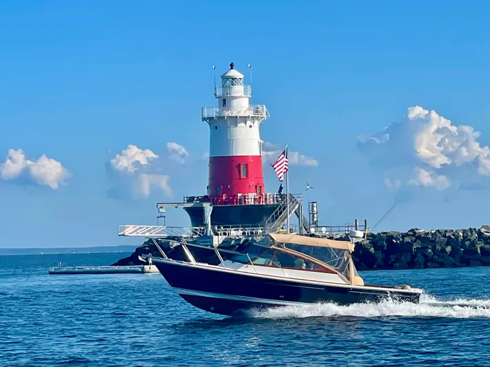  Yacht Photos Pics 2009 Hunt Yachts Harrier 29 cruising near a lighthouse under a clear blue sky.