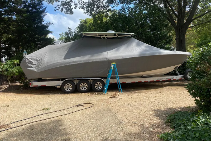  Yacht Photos Pics Covered 2023 Statement 350 Open boat on trailer, surrounded by trees and a ladder nearby.