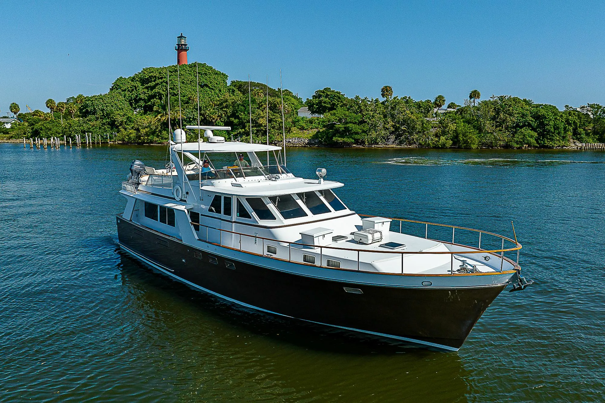 1986 Tollycraft Pilothouse yacht cruising near a lush, green shoreline with a lighthouse in the background.