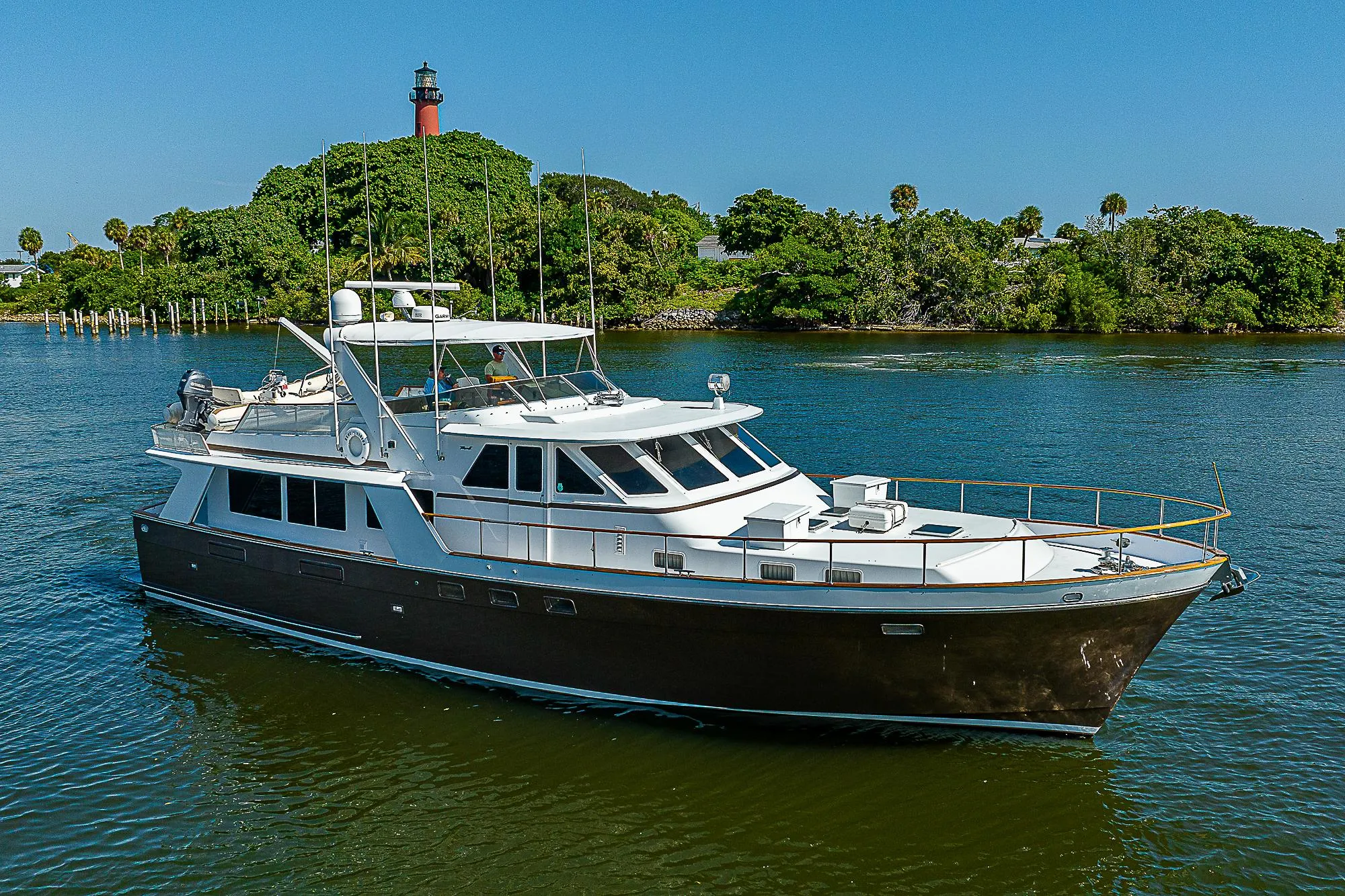 1986 Tollycraft Pilothouse yacht cruising on a serene waterway with lush greenery and a lighthouse in the background.