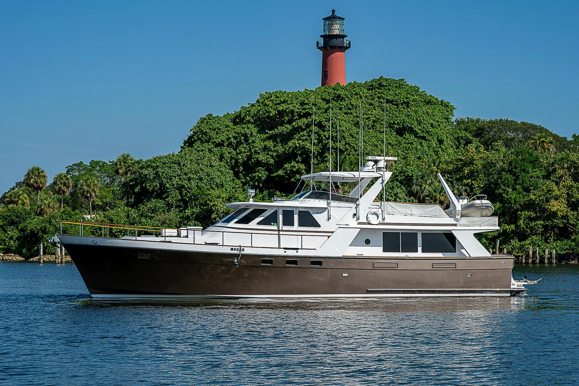 1986 Tollycraft Pilothouse yacht cruising near a lighthouse and lush greenery.
