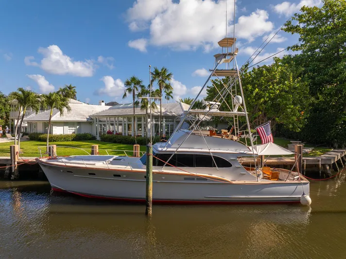 Ta-boo Yacht Photos Pics Vintage 1970 Rybovich 54 yacht docked by a waterfront home, under a clear blue sky.