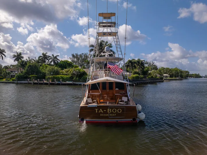 Ta-boo Yacht Photos Pics 1970 Rybovich 54 yacht on a serene waterway, American flag displayed, surrounded by lush greenery.
