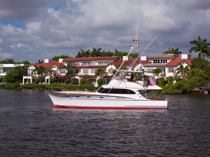 Ta-boo Yacht Photos Pics 1970 Rybovich 54 yacht cruising near luxury waterfront homes under a partly cloudy sky.