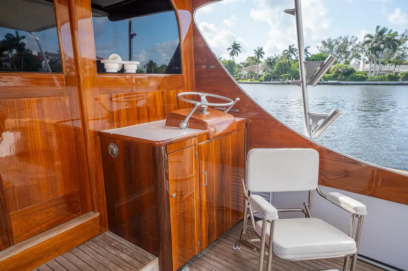 Ta-boo Yacht Photos Pics 1970 Rybovich 54 yacht interior with polished wood, steering wheel, and white chair by the water.