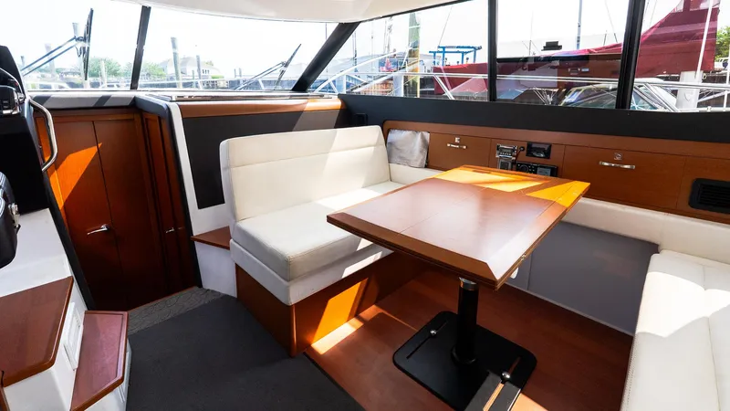  Yacht Photos Pics 2018 Jeanneau NC11 interior with dining area, white seating, and wooden table.