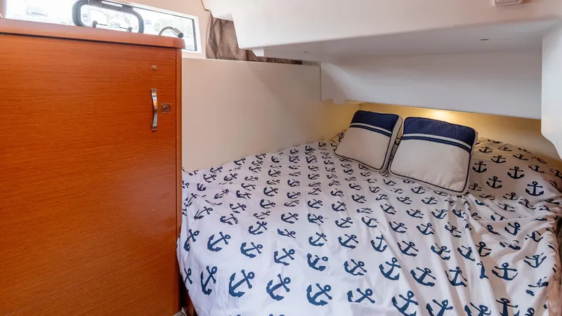  Yacht Photos Pics Cozy cabin interior of 2018 Jeanneau NC11 with anchor-patterned bedding and wooden cabinet.