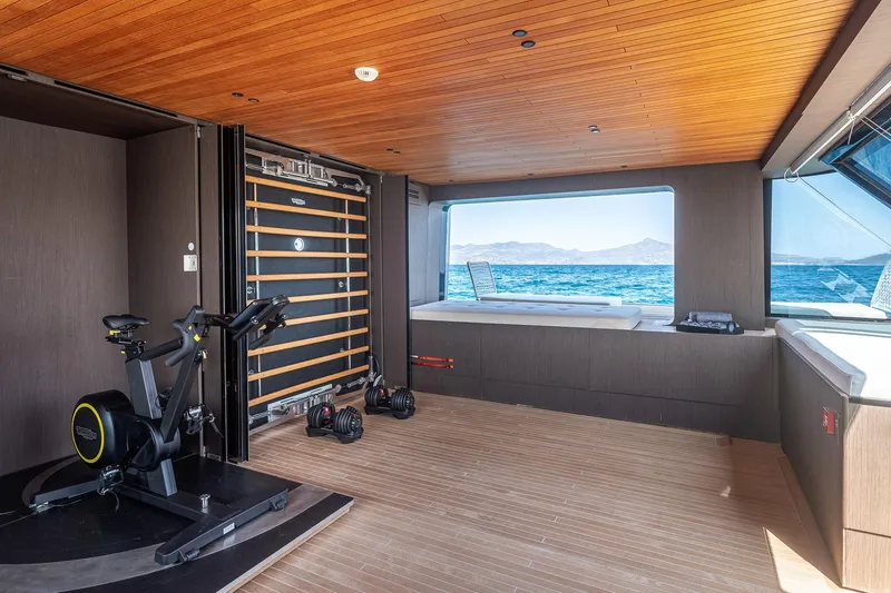 Just Marie 3 Yacht Photos Pics Luxurious 2021 Sanlorenzo SX112 yacht gym with exercise bike, sea view, and wooden interior.