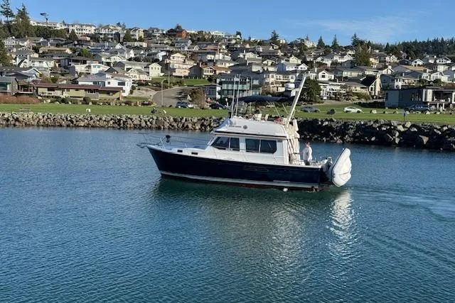 Ocean Baron Yacht Photos Pics 2001 Sabreline Sedan boat cruising near a coastal town with houses in the background.