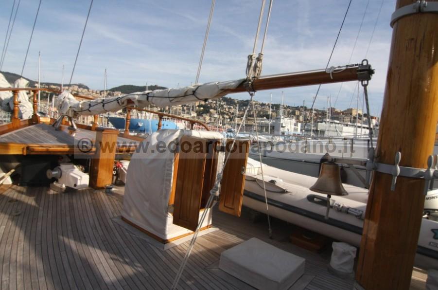 1925 Codecasa schooner deck with wooden masts and rigging in a marina setting.