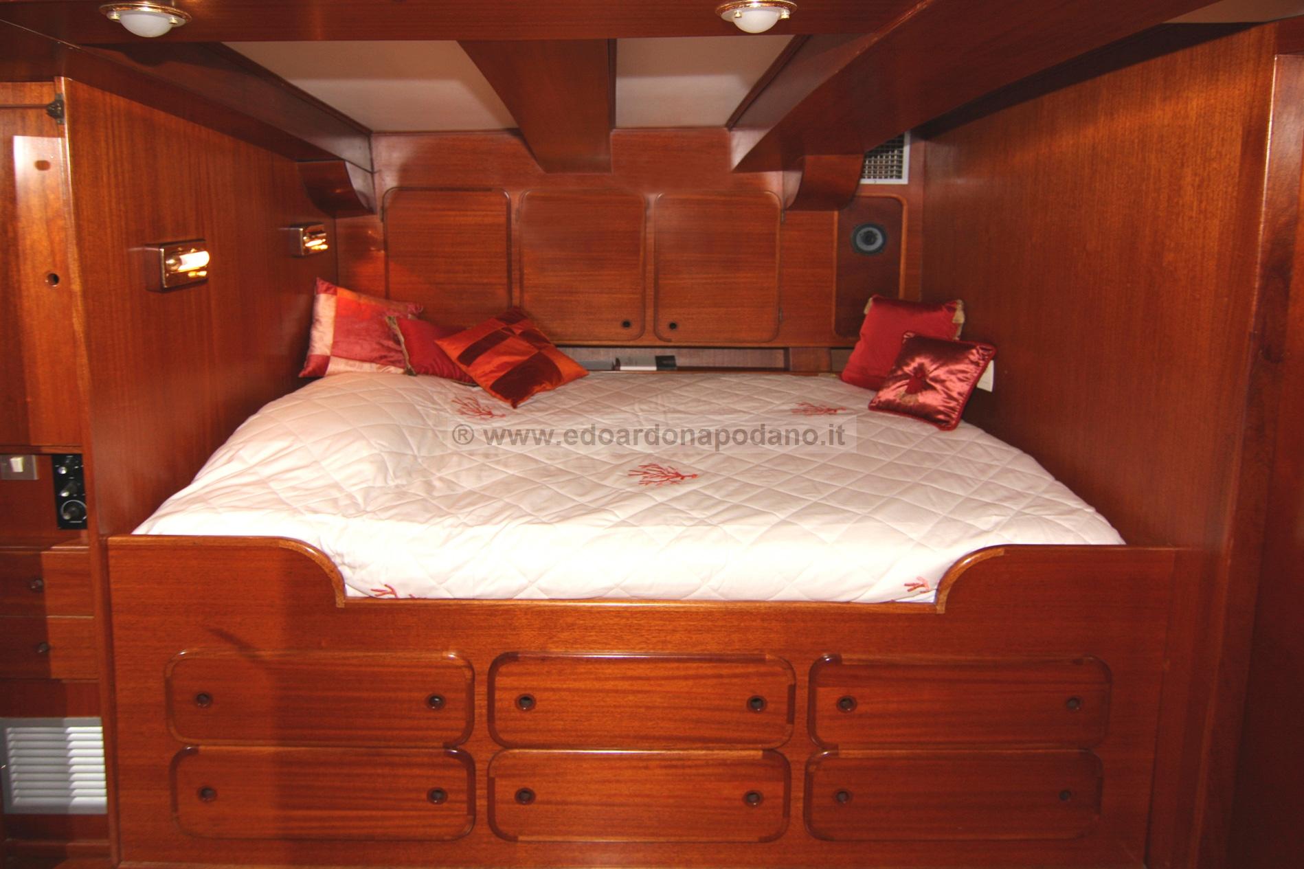 Luxurious wooden cabin interior of 1925 Codecasa schooner with cozy bed and red pillows.