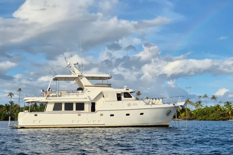Beyond Capricorn 1 Yacht Photos Pics 2001 Nordhavn 57 yacht on calm water with palm trees and cloudy sky.